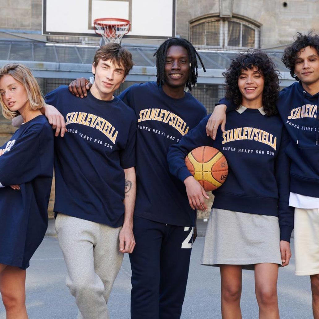 Eine Gruppe von fünf Menschen steht am Basketballplatz, alle tragen dunkelblaue Kleidung mit Stanley/Stella Aufschrift