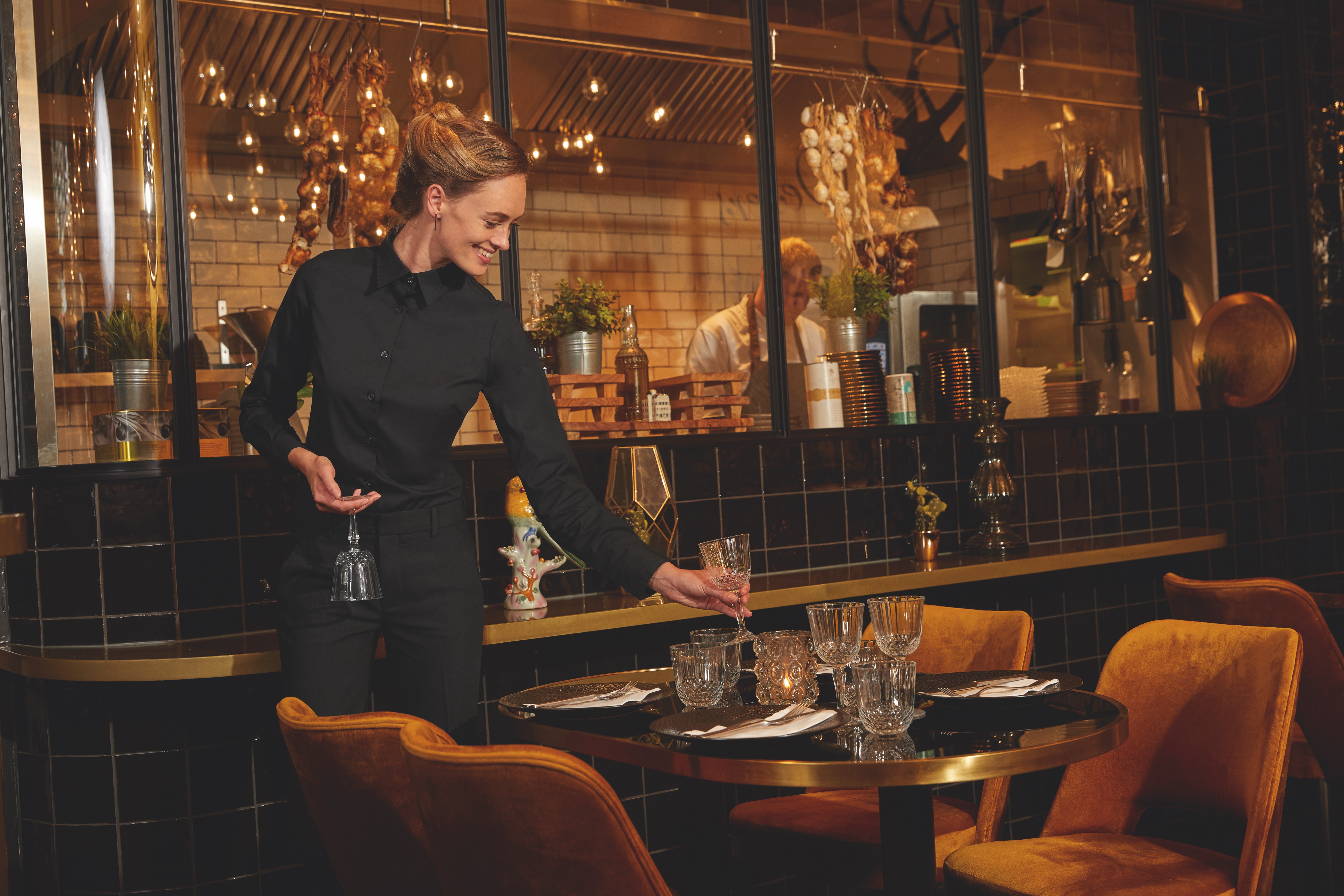 Kellnerin in schwarzem Outfit, stellt Glas auf Tisch